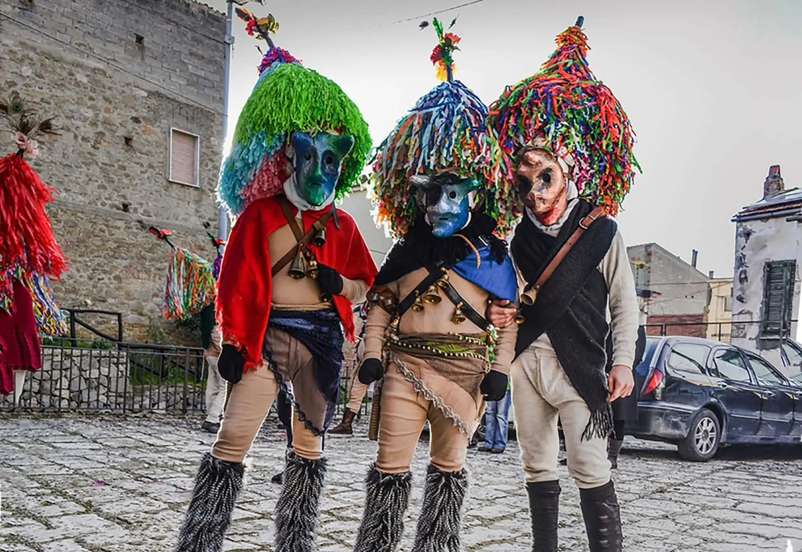 Tre Maschere Cornute di Aliano in piedi lungo la strada, con i grandi cappelloni di frange colorate
