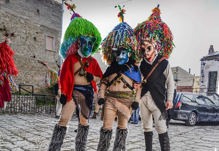 Tre Maschere Cornute di Aliano in piedi lungo la strada, con i grandi cappelloni di frange colorate