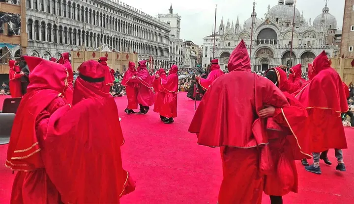 I Domini di Lavello in mantella rossa riuniti in una piazza monumentale durante una sfilata fuori dal paese