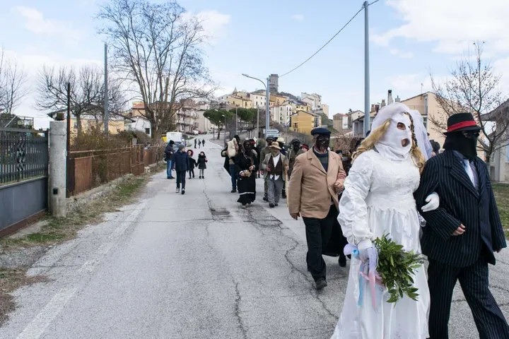 Il corteo del Carnevale di Teana lungo la strada: figuranti in abito scuro accompagnano una maschera vestita di bianco