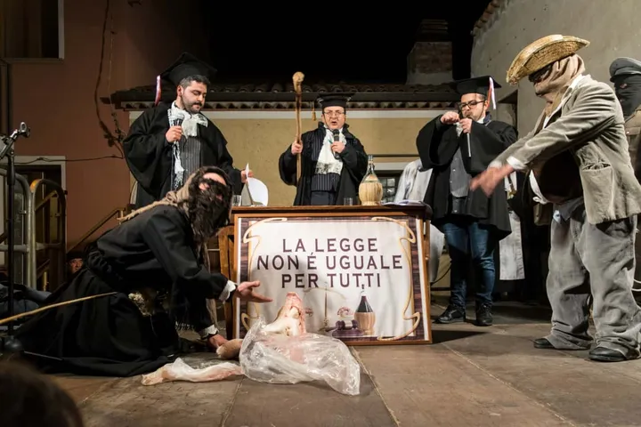 Il Processo a Carnuluvar: giudice e avvocati dietro un cartello con la scritta «La legge non è uguale per tutti»