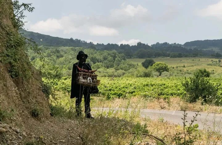 Una figura ammantata di scuro cammina nella campagna intorno a Teana, fra i filari e le colline